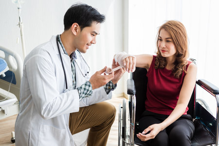 man doctor with wrapping nurse bandages splint to the arm of a female patient wear arm splint with analogue pressure gauge for better healing In the room hospital background.の写真素材