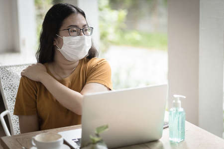 freelance people business female wearing protective mask casual suffers from shoulder pain from working with laptop computer ,working from home,Concept of Prevention of the spread of COVID-19 virusの写真素材