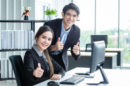 Happy of businesswoman and businessman partners showing thumbs up discussing positive adult business working together with computer on wooden table and ideas at meeting in office background.の写真素材