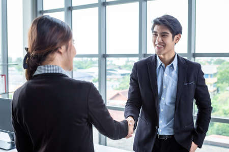 Asian businesswoman and businessman shaking hands at In the office room background after the contract is signed or handshake greeting deal,business expressed confidence embolden and successful coupleの写真素材
