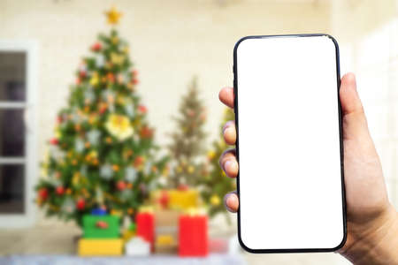 Close-up of female use smartphone blurred images with Colorful balls on Green Christmas tree background Decoration During Christmas and New Year.の写真素材