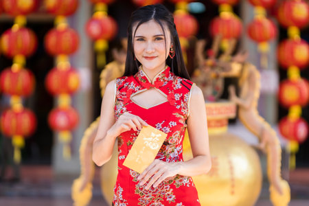 Portrait Asian young woman wearing red traditional Chinese cheongsam decoration holding yellow envelopes with the Chinese text Blessings written on it Is a Good luck for Chinese New Year Festivalの写真素材