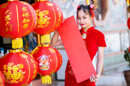 little Asian girl wearing red traditional Chinese cheongsam decoration show blank paper red and lanterns with the Chinese text Blessings written on it Is a Fortune blessing for Chinese New Yearの写真素材