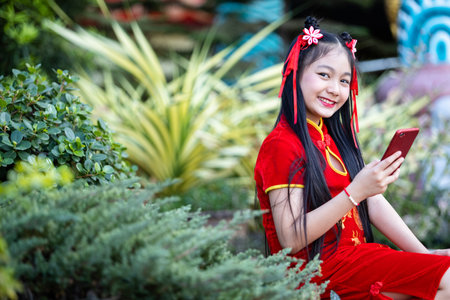 Portrait beautiful smiles Cute little Asian girl wearing red traditional Chinese cheongsam decoration taking a selfie with smartphone for Chinese New Year Festival at Chinese shrineの写真素材