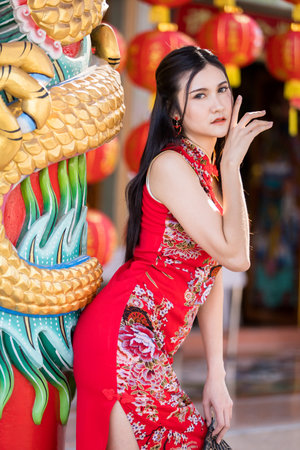 Portrait beautiful smiles Asian young woman wearing red traditional Chinese cheongsam decoration for Chinese New Year Festival at Chinese shrine in Thailandの写真素材