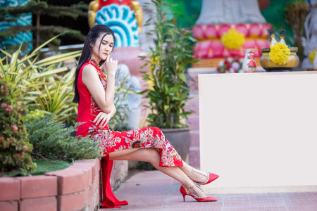 Portrait beautiful smiles Asian young woman wearing red traditional Chinese cheongsam decoration for Chinese New Year Festival at Chinese shrine in Thailandの写真素材