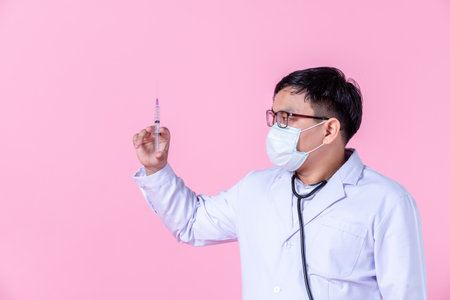 Asian man doctor therapeutic,stethoscope advising with positive emotions advising with arms folded and holding a syringe to the side eyes looking at camera in isolated on pink blank copy spaceの写真素材