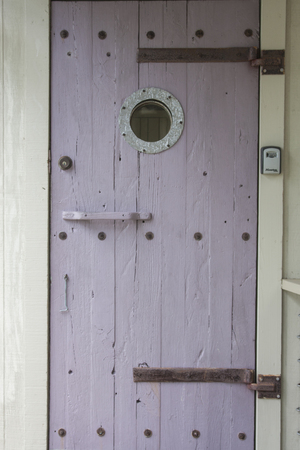 A weathered wooden ship door with a portholeの写真素材