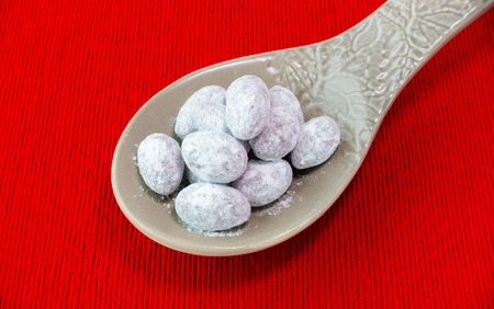 A heap of icing sugar and chocolate coated Christmas almonds on a big grey ceramic spoon isolated on red textile background.の写真素材