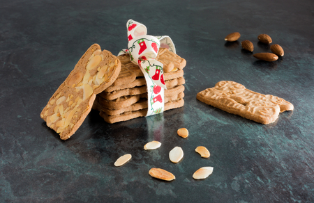 Closeup of a stack of spiced biscuits with almonds ( Spekulatius ) decorated with Christmas Bow, surrounded by almonds on black background.の写真素材