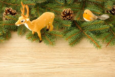 Christmas Scene and Christmas Border with Reindeer, Robin Bird, Pine Cones and Fir Tree Twigs on light brown wooden background with copy space.の写真素材