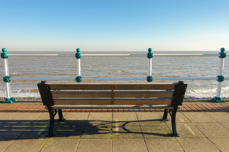 Empty wooden bench on a promenade overlooking the sea on a sunny day in winter.の写真素材