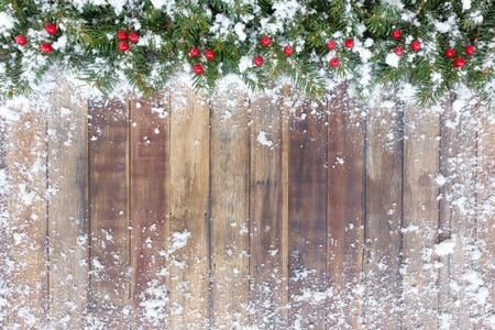 Christmas border out of natural Christmas tree fir twigs and red berries on a brown wooden background covered in snow with copy space.の写真素材