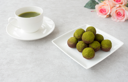 Homemade matcha chocolates, a cup of green matcha tea and a bouquet of pink roses on light gray textured background.の写真素材