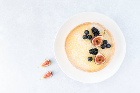 Top view of a lemon tart decorated with figs, blueberries and blackberries on light blue background with copy space.の写真素材