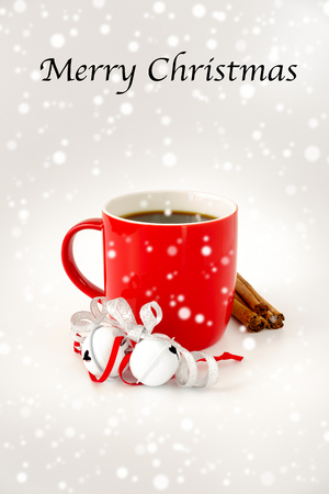 Red Christmas mug filled with black coffee and decorated with white jingle bells, silver metallic ribbon, cinnamon sticks and snowfall. Merry Christmas written on the top.の写真素材