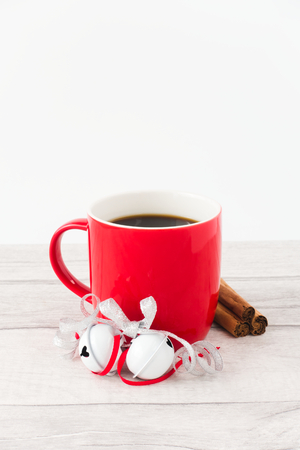 Red mug filled with black coffee ,decorated with white jingle bells, silver metallic ribbon, and a mince pie on gray wood and white background. Angled view and copy space.の写真素材