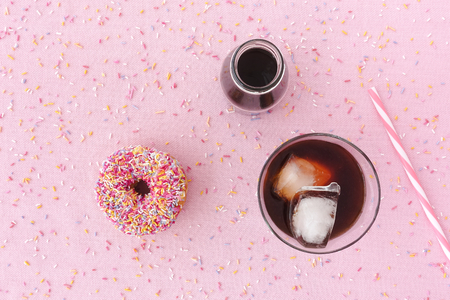 Pink frosted donut with colorful sprinkles, a glass filled with cold brew coffee, cold brew coffee concentrate in a milk bottle and a straw on pink background with multi colored sprinkles. Top view.の写真素材