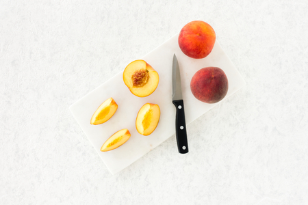 Whole and cut peaches and a knife on marble chopping board and white, gray, textured and patterned background. Top view.の写真素材