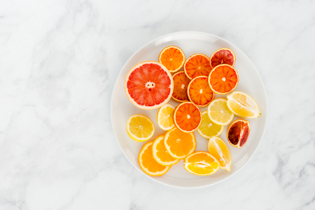Cut oranges, blood oranges, lemon and grapefruit on a large white plate and white marble background with lots of copy space. Top view.の写真素材
