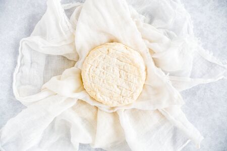 Round soft cow cheese on white muslin cloth and blue patterned background. Top view.の写真素材
