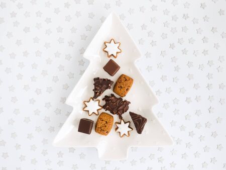 German gingerbreads, Lebkuchen , on tree shaped Christmas serving plate and white background covered with silver confetti stars. Top view.の写真素材
