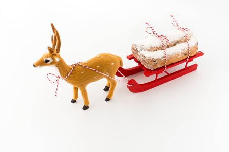 Deer pulling a red wooden sledge with stollen, a German Christstollen, isolated on white. Angled view.の写真素材