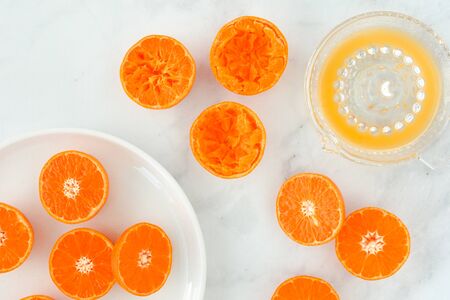 Close-up of citrus fruits, clementines, cut in half on plate and glass citrus juicer filled with...
