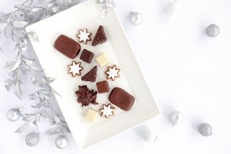 Assortment of German gingerbread, Lebkuchen, on white serving plate with silver leaf garland and silver Christmas baubles on white background. Top view.の写真素材