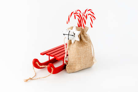 Sledge and candy canes in jute sack with jingle bells and Christmas star isolated on white with copy space.の写真素材