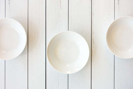 Three white empty porcelain bowls on white wooden plank background. Top view.の写真素材