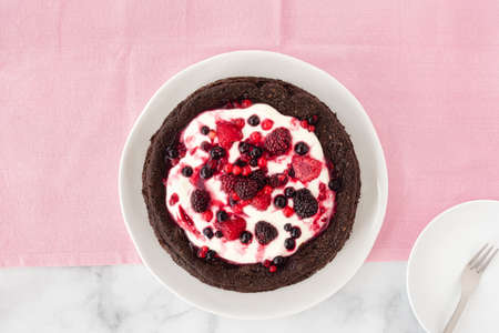 Top view of a chocolate cloud cake, flourless, with creme fraiche and frozen summer berries on pink tablecloth. Vertical version.の写真素材