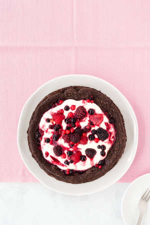 Homemade chocolate cloud cake, flourless, with creme fraiche and frozen summer berries on pink tablecloth. Top view. Horizontal version.の写真素材
