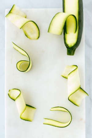 Courgette, zucchini ribbons and courgette, zucchini on white marble board with copy space. Top view.の写真素材