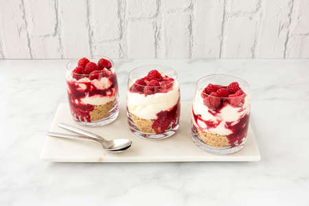 Homemade raspberry dessert in three glasses on white marble with white brick wall in the background. Angled view and copy space.の写真素材