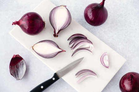 Red raw onions, whole, halved, quartered and sliced on white marble chopping board with knife. High angle view and copy space.の写真素材