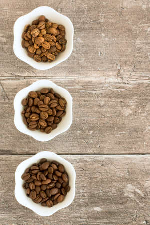 Light roast, medium roast and dark roast speciality arabica beans in white bowls over brown weathered wood with copy space. Top view.の写真素材