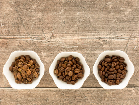 Light roasted, medium roasted and dark roasted speciality arabica beans in white bowls over brown weathered wood with a lot of copy space. Top view.の写真素材