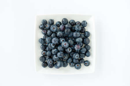 Top view of fresh blueberries on a white square porcelain plate isolated on white. Copy space.の写真素材