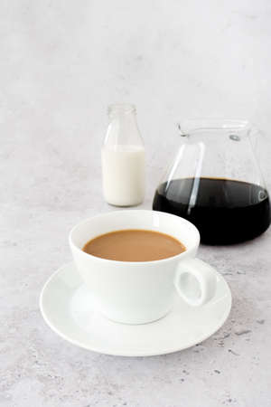 Cup of milk coffee with coffee pot and a bottle of milk in the background. Low angle view. Shallow depth of field.の写真素材