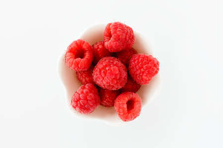 Closeup of fresh raspberries in a cute white bowl isolated on white background. Top view.の写真素材