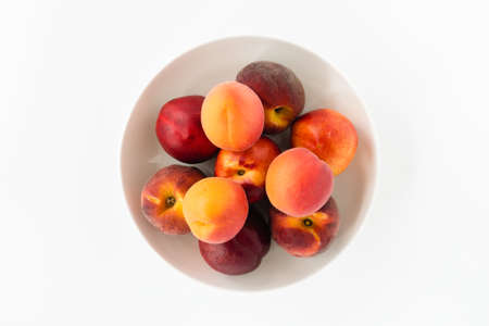 Top view of fresh, whole peaches, nectarines and apricots in a white porcelain bowl isolated on white.の写真素材