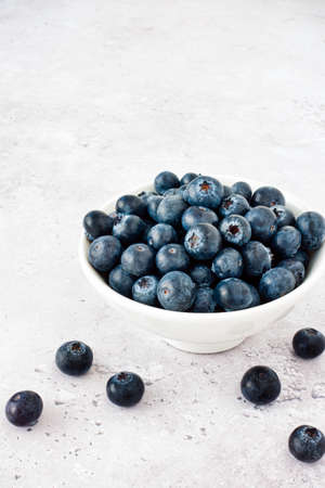 Close-up of fresh blueberries in a white bowl on a grey stone background with copy space. Angled view.の写真素材
