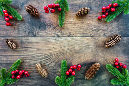 Christmas frame with fir branches and red berries as decoration on dark brown weathered wood with copy space. Top view.の写真素材
