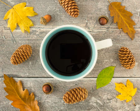 Top view of a mug filled with black coffee, fall leaves, pinecones and acorns on weathered wood panel background.の写真素材