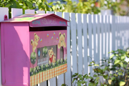 A pink mail box on white fenceの写真素材