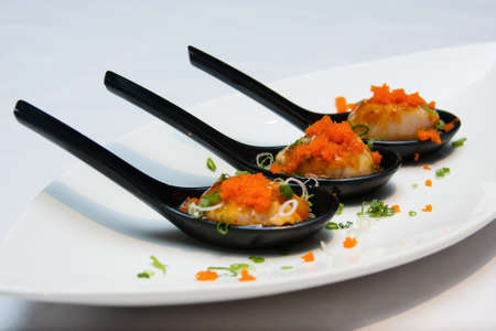 scallops on black spoon topped with fish eggsの写真素材