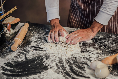 Man preparing buns at table in bakery, Man sprinkling flour over fresh dough on kitchen tableの写真素材