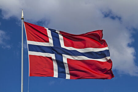 Norwegian flag fluttering in the wind against a blue cloudy skyの写真素材