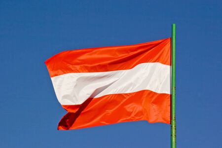 Austrian flag flutters in front of blue cloud sky in the wind